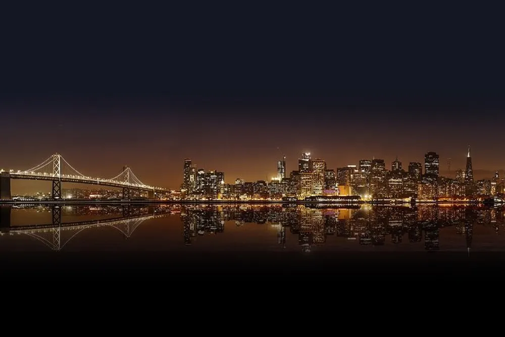 The image depicts a nighttime city skyline with brightly illuminated buildings and a bridge reflected over a body of water creating a symmetrical view