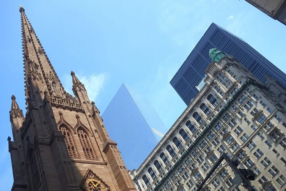 The image shows a contrast of architectural styles with an ornate gothic church spire in the foreground and modern skyscrapers in the background under a blue sky