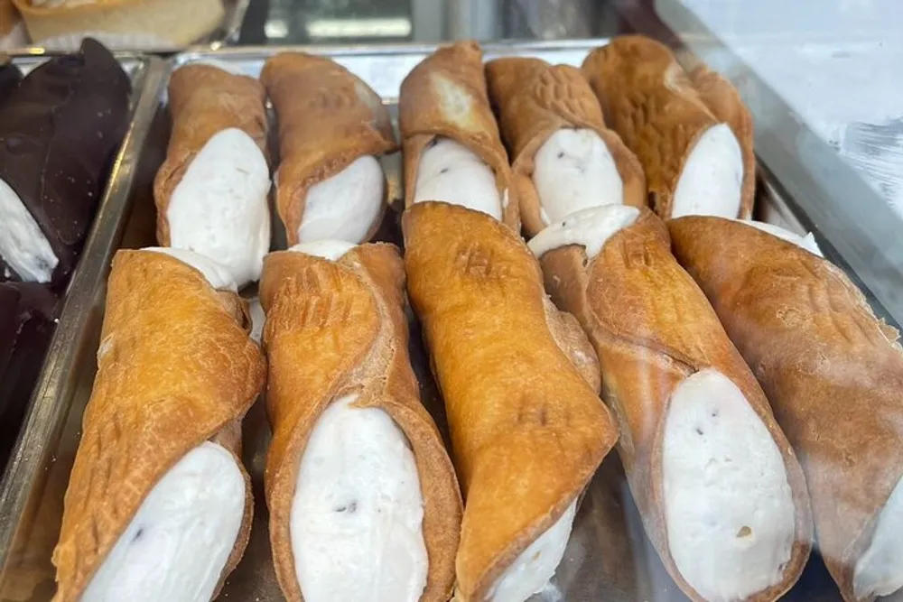 The image shows a display of cannoli a traditional Italian dessert consisting of tube-shaped shells of fried pastry dough filled with a sweet creamy filling containing ricotta cheese