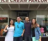Four people are smiling in front of an old-fashioned ice cream parlor that also advertises homemade chocolates and luncheon services