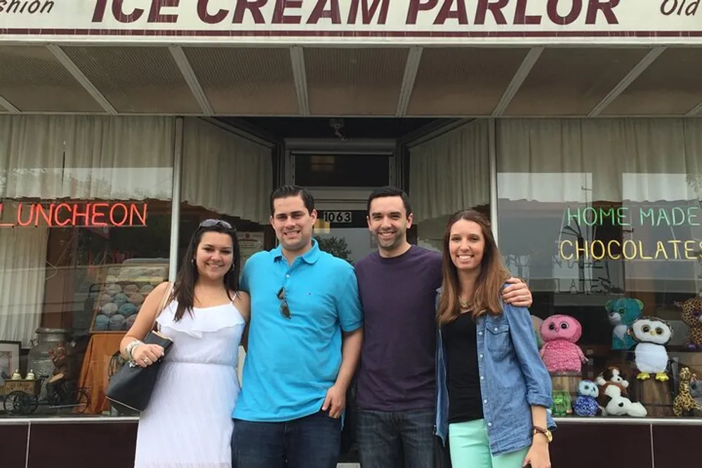 Four people are smiling in front of an old-fashioned ice cream parlor that also advertises homemade chocolates and luncheon services