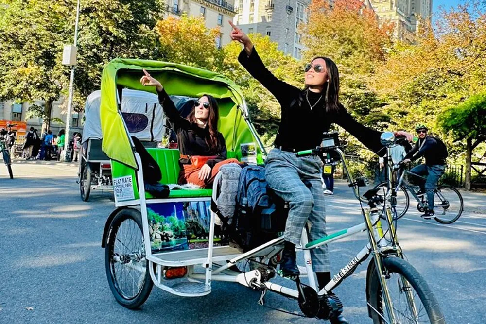 A passenger in a green rickshaw is pointing upwards while the cyclist navigates through a bustling street with bicycles in the background
