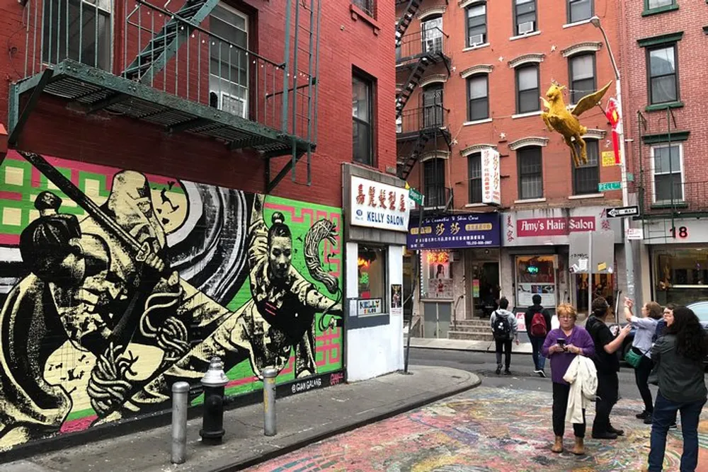 This image shows a lively urban street corner with a large black and white mural a golden statue on a rooftop and pedestrians engaged in conversation