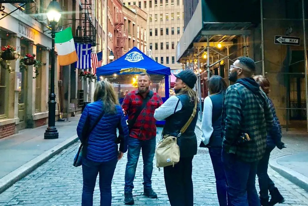 A group of people are engaging in conversation on a cobbled street with festive decorations and tents in the background