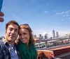 A smiling couple is taking a selfie with a city skyline including a tall skyscraper in the background