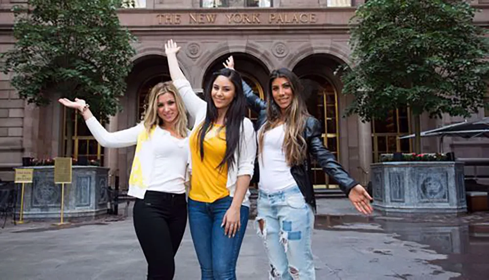 Three women are smiling and posing in front of the New York Palace Hotel