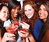 Four smiling women are holding and toasting with red cocktails at a bar