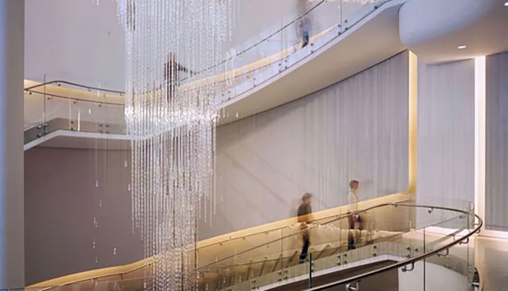 The image shows an elegant interior space with a cascading modern chandelier curving staircases and blurred figures of people suggesting movement within the serene architectural setting