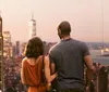 A couple is enjoying a scenic view of a city skyline at dusk with notable skyscrapers and water bodies in the distance
