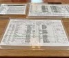 The image shows a set of printed papers possibly documents or records enclosed in clear protective sleeves lying on a wooden table