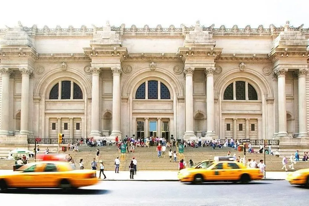 This is a bustling scene in front of a grand neoclassical building with people ascending its steps and yellow taxicabs passing by in the foreground