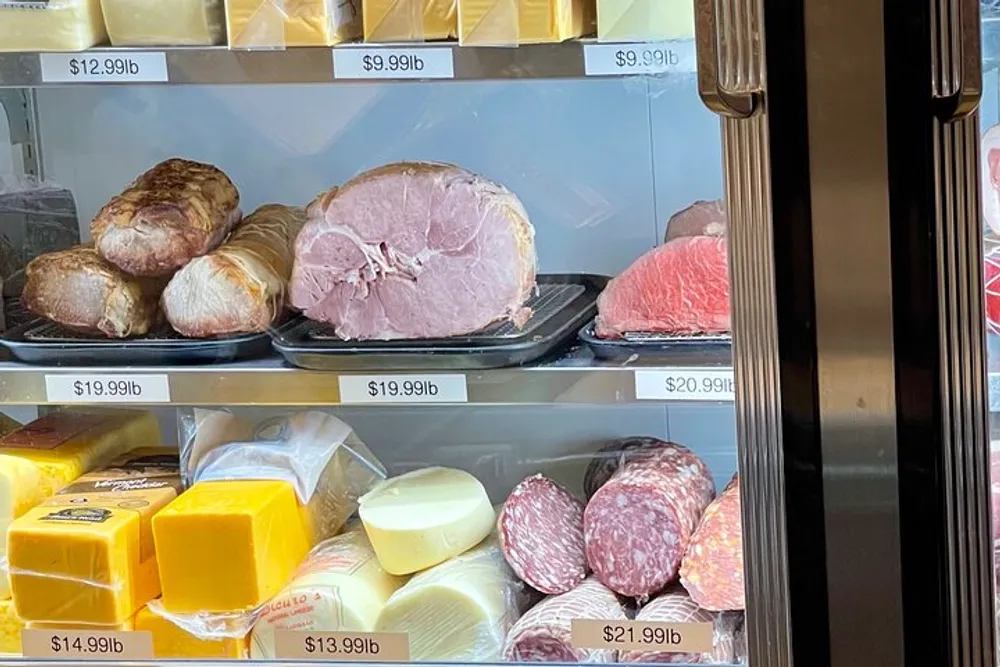 The image shows an open refrigerated display case stocked with various types of meats and cheeses each labeled with a price per pound