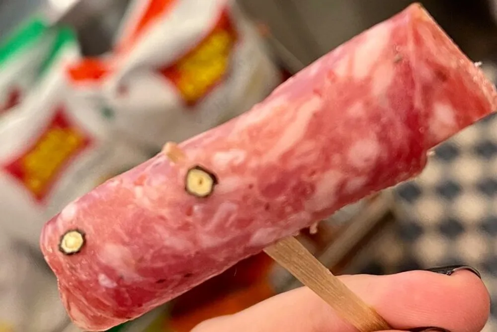 A person is holding a popsicle that humorously resembles a piece of raw marbled meat on a wooden stick