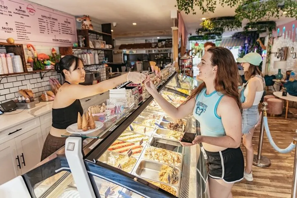 A customer is receiving a cone of ice cream from an employee at a brightly decorated ice cream shop