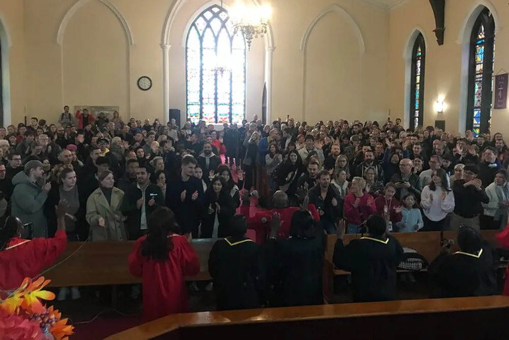 A diverse group of people is gathered inside a church clapping and appearing to be engaged in a celebratory or significant event