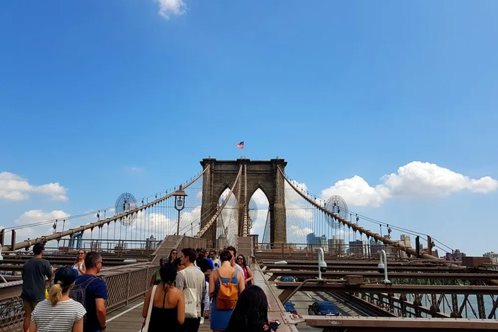 Tourists are walking across the Brooklyn Bridge on a sunny day with clear blue skies