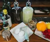The image displays various cocktail ingredients and tools including citrus fruits berries eggs bitters syrups and a juicer arranged on a bar counter