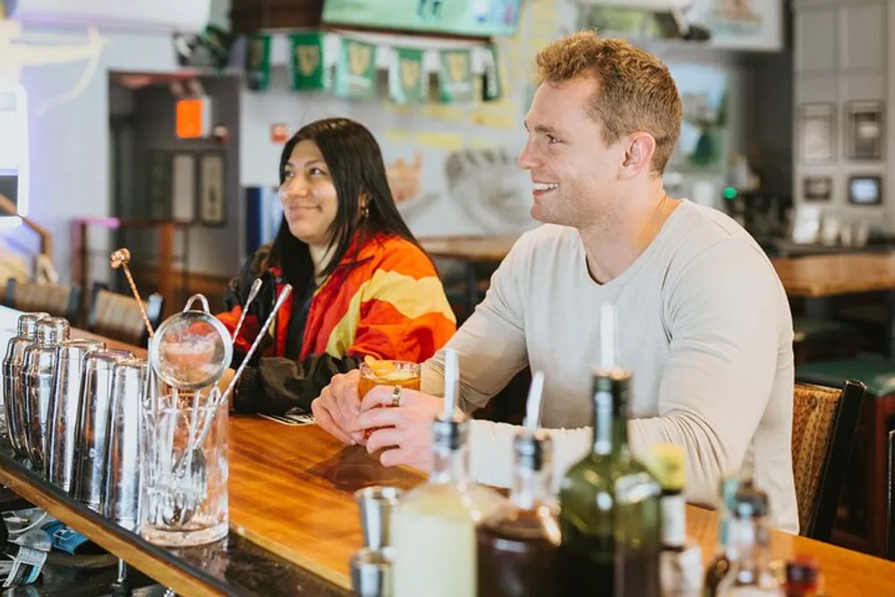 Two people are sitting at a bar with drinks smiling and enjoying each others company