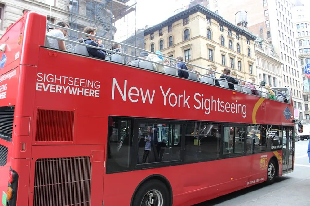 A red double-decker sightseeing bus filled with tourists explores the streets of New York City