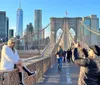 A person poses for a photo while another takes their picture on Brooklyn Bridge with the New York City skyline in the background