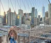 A person poses for a photo while another takes their picture on Brooklyn Bridge with the New York City skyline in the background