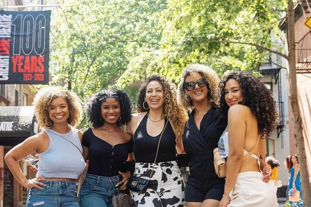 Five smiling women pose together on a sunny city street exuding friendship and style
