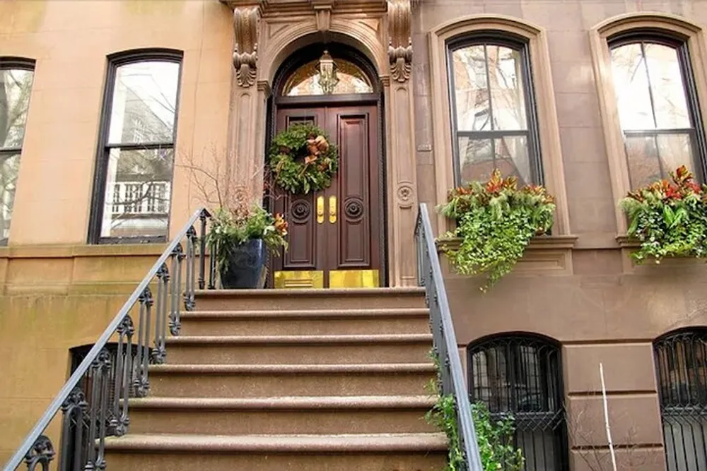 The image shows the ornate entrance of a brownstone building flanked by green plants and decorative elements leading up a set of stone steps