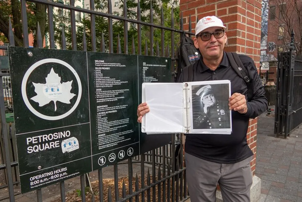 A man is holding open a book with a photograph next to a sign for Petrosino Square