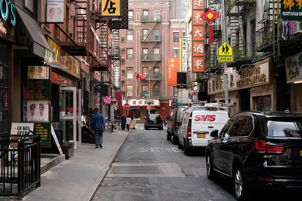 This image captures a bustling street scene in Chinatown with pedestrians vehicles and various signs in Chinese characters adorning the buildings