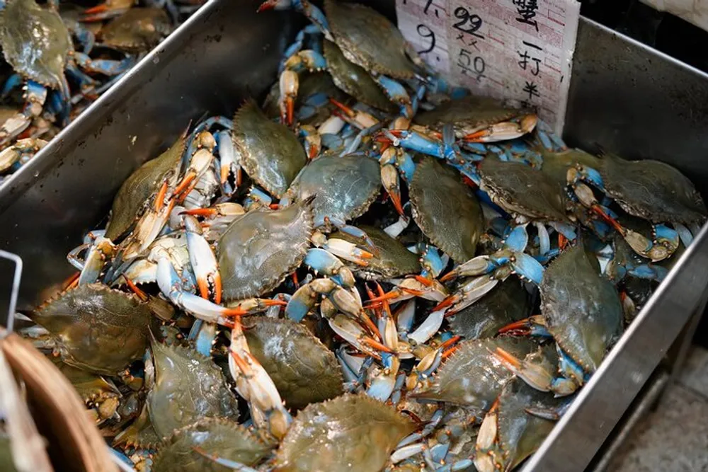The image shows a tray filled with blue crabs for sale at a market with a price tag indicating they are 950 units of currency per pound