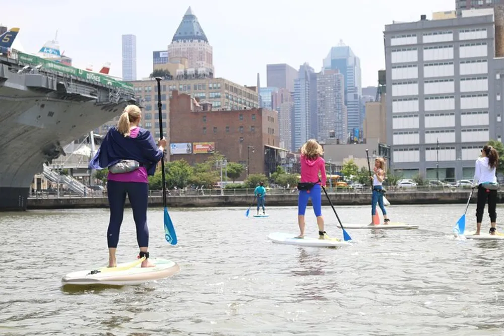 People are paddleboarding on the water with a city skyline and a large ship in the background