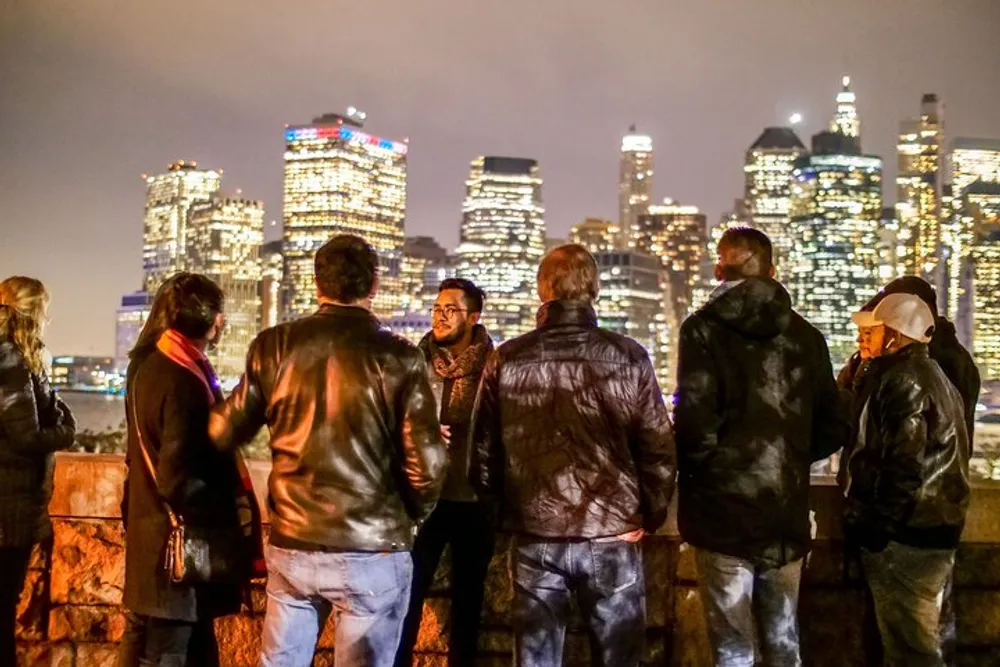 A group of people are enjoying a conversation against the backdrop of a brightly lit city skyline at night