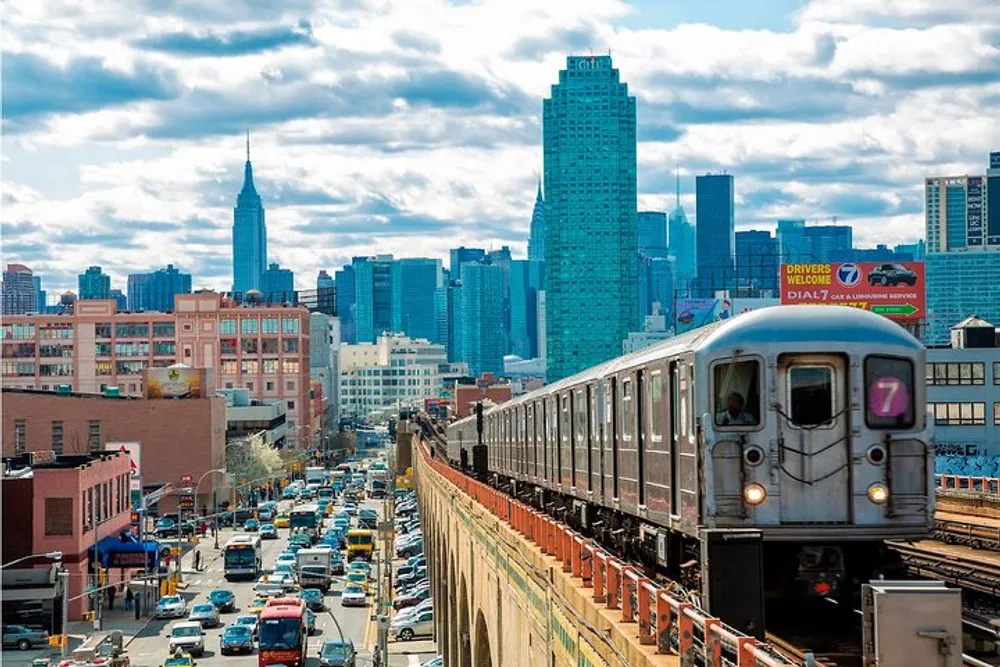 A train travels on elevated tracks above a bustling street with the New York City skyline in the background