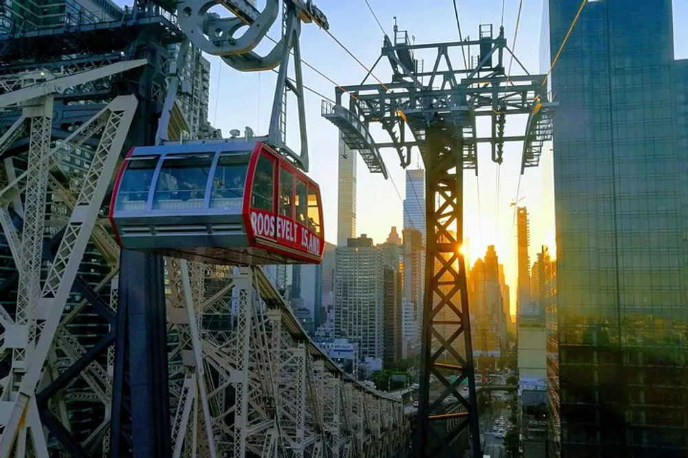 An aerial tramway cabin traverses above a cityscape against the backdrop of a sunset