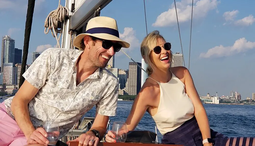 Two people are sharing a joyful moment while sailing on a sunny day with a city skyline in the background