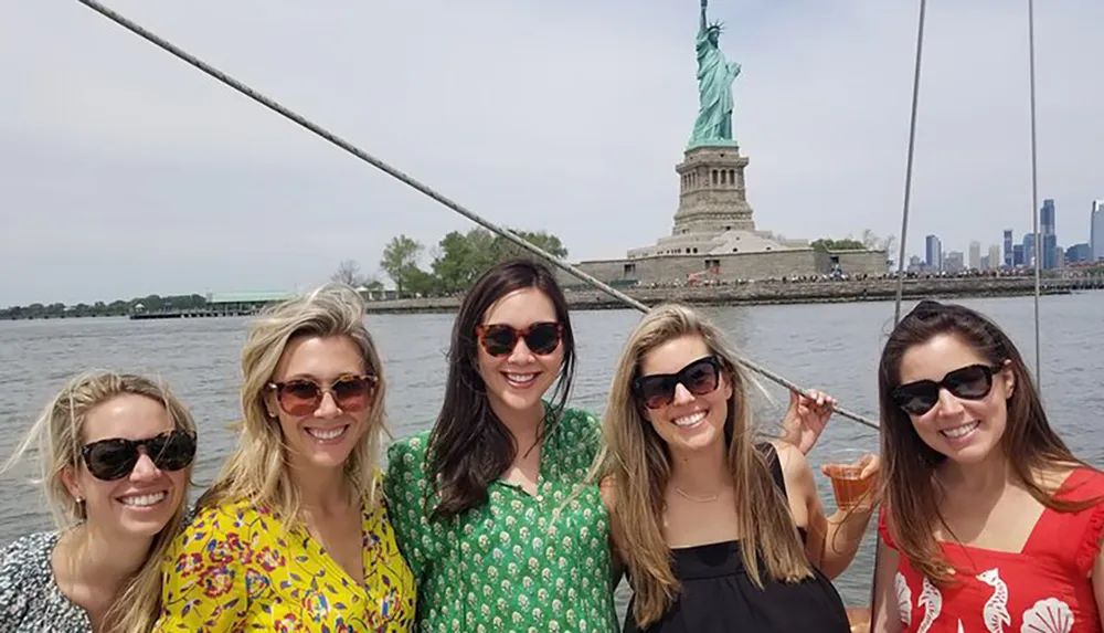 A group of smiling individuals on a boat pose for a photo with the Statue of Liberty in the background