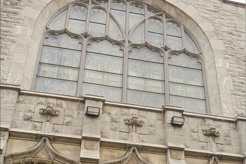 This image shows an ornate Gothic-style stained glass window on a stone building with arches and decorative stone carvings