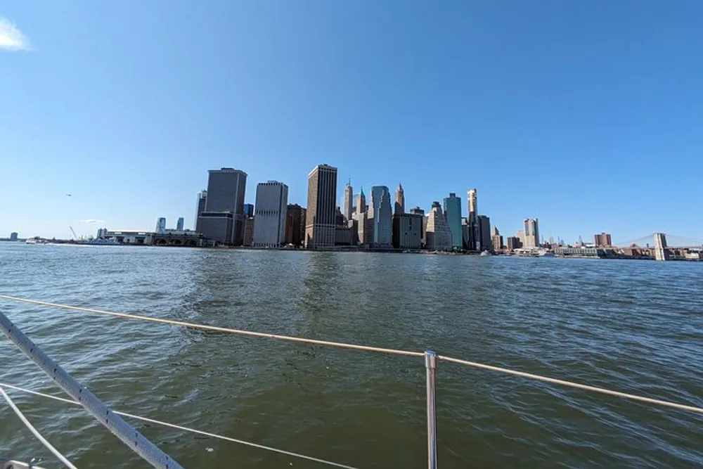 The image shows a panoramic view of a city skyline from the perspective of a boat on the water featuring high-rise buildings under a clear blue sky