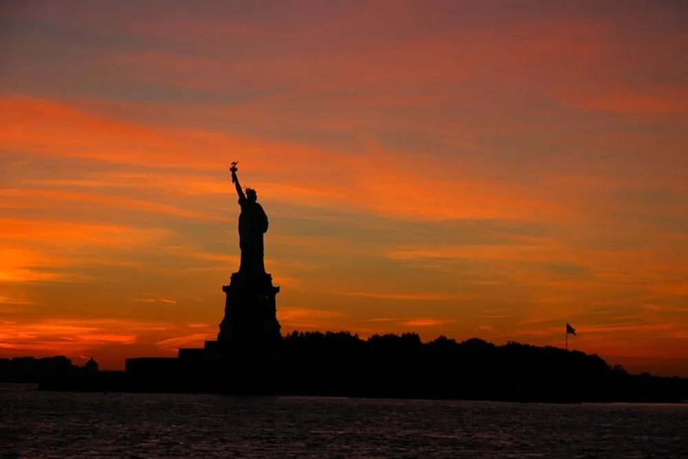 The Statue of Liberty is silhouetted against a vibrant sunset sky