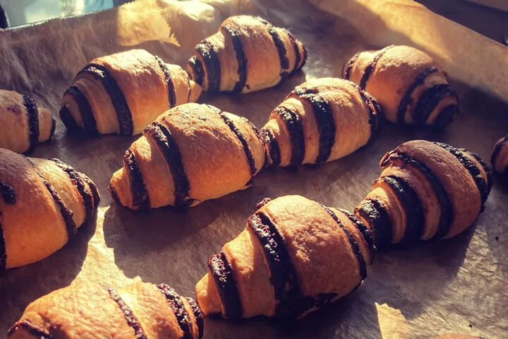The image shows freshly baked croissants with chocolate drizzle casting shadows in warm sunlight