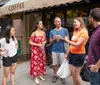 A group of six people is engaging in a lively conversation on a city sidewalk outside a coffee shop
