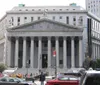 The image shows the imposing facade of a neoclassical courthouse with large columns pedestrians and vehicles in the foreground