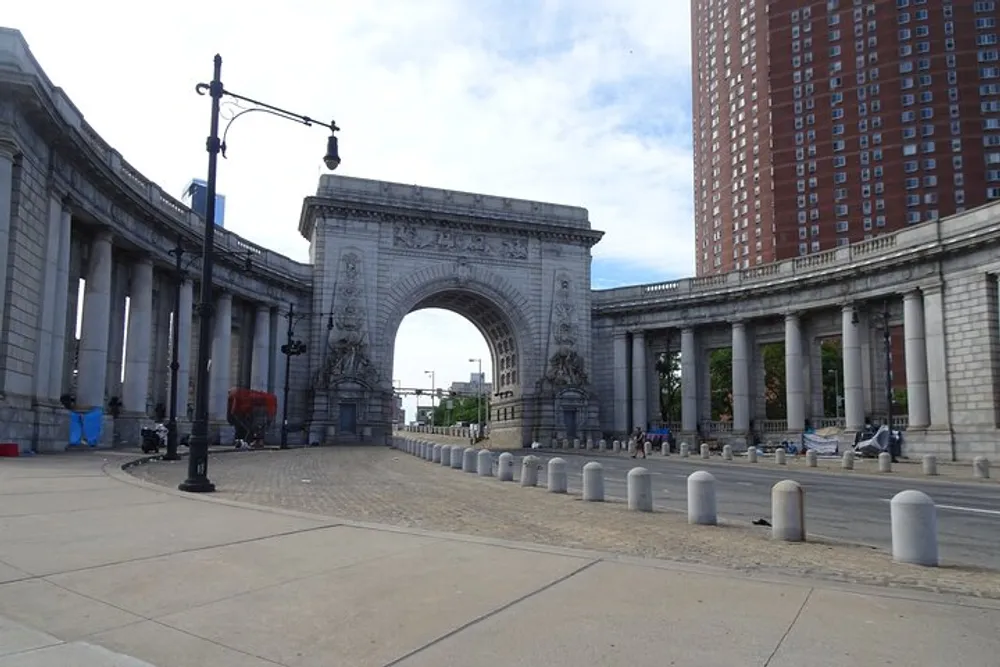 The image features a spacious and ornate arch structure flanked by columns situated in an urban setting with clear skies overhead