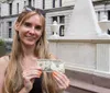 A smiling woman is holding a ten-dollar bill in front of the Alexander Hamilton memorial