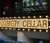 The image shows a lit-up marquee with the words COMEDY CELLAR suggesting it is the entrance to a comedy club