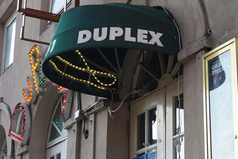 The image shows an outdoor awning with the word DUPLEX above a door adorned with a lit neon sign shaped like a cocktail glass