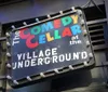 The image shows a lit-up marquee with the words COMEDY CELLAR suggesting it is the entrance to a comedy club