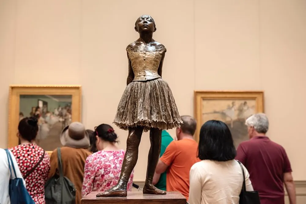 A group of museum visitors is looking at paintings with their attention seemingly directed away from a prominent bronze sculpture of a ballet dancer positioned in the foreground