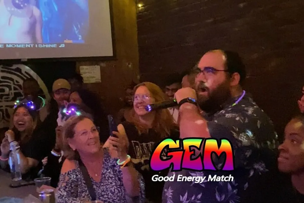 A man is singing at a karaoke event while an enthusiastic crowd some with flashing headwear watches and captures the moment on their phones