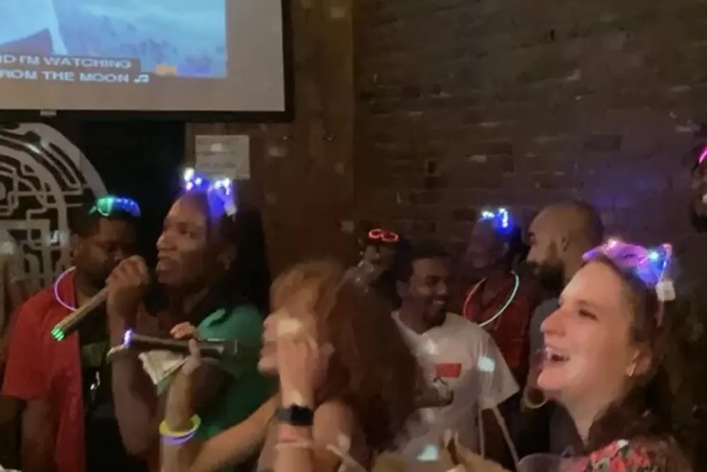 A group of people is enjoying a lively party atmosphere some wearing glowing head accessories with a karaoke machine in the background